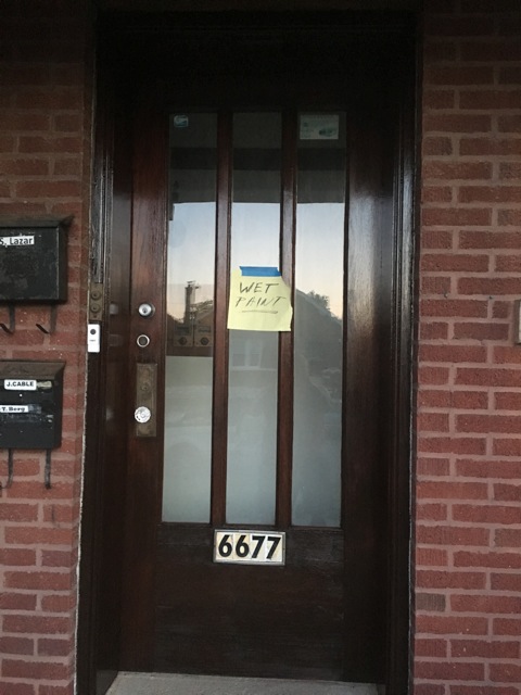 A dark door with the number "6677" with a hand written yellow paper "WET PAINT"